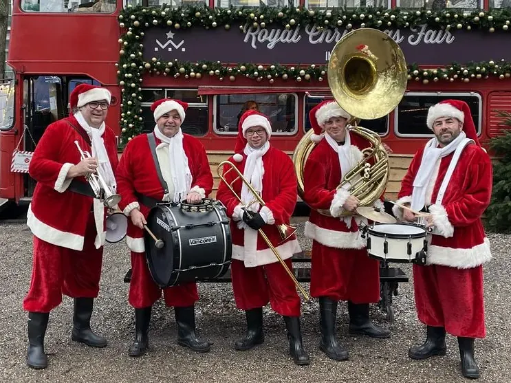 Dixielandband in kerstpakken met trompet, trommels en sousafoon voor een rode dubbeldekkerbus
