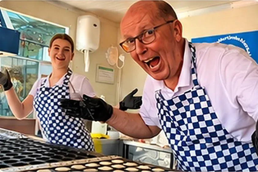 Enthousiaste bakker in een geblokt schort bij de poffertjeskraam